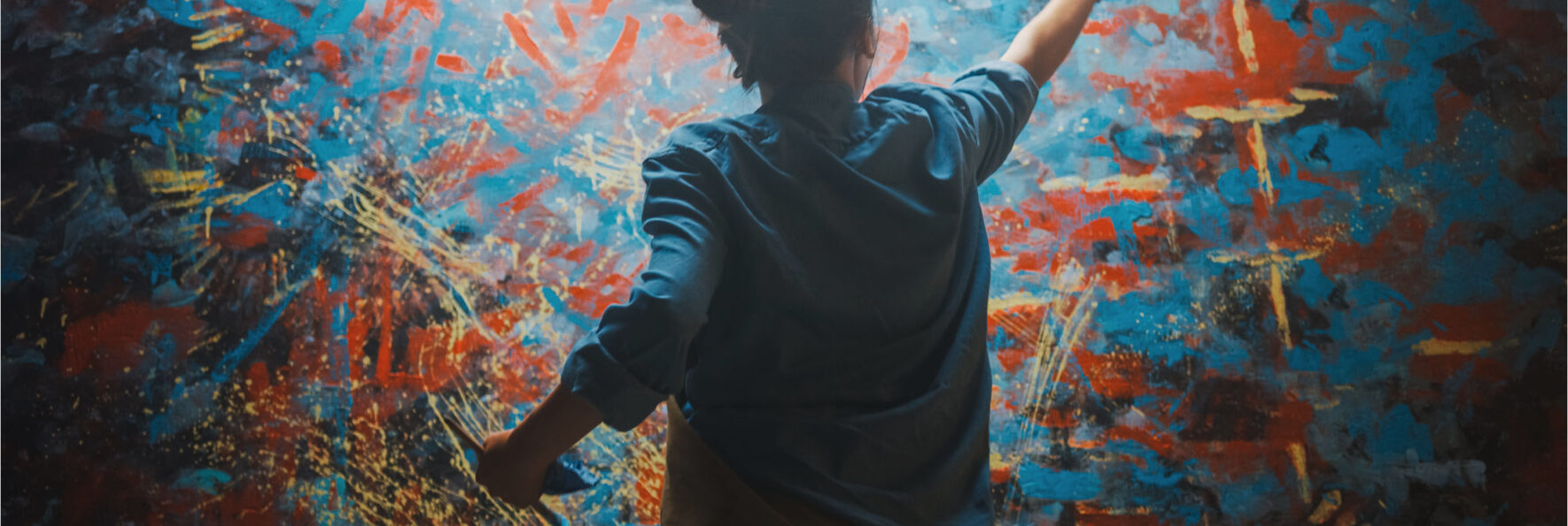 Talented Female Artist Works on Abstract Oil Painting, Using Paint Brush She Creates Modern Masterpiece. Dark and Messy Creative Studio where Large Canvas Stands on Easel Illuminated.