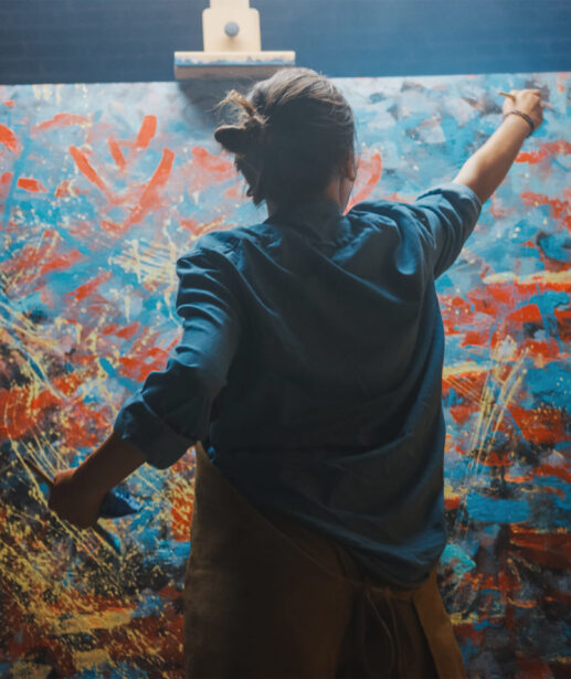 Talented Female Artist Works on Abstract Oil Painting, Using Paint Brush She Creates Modern Masterpiece. Dark and Messy Creative Studio where Large Canvas Stands on Easel Illuminated.