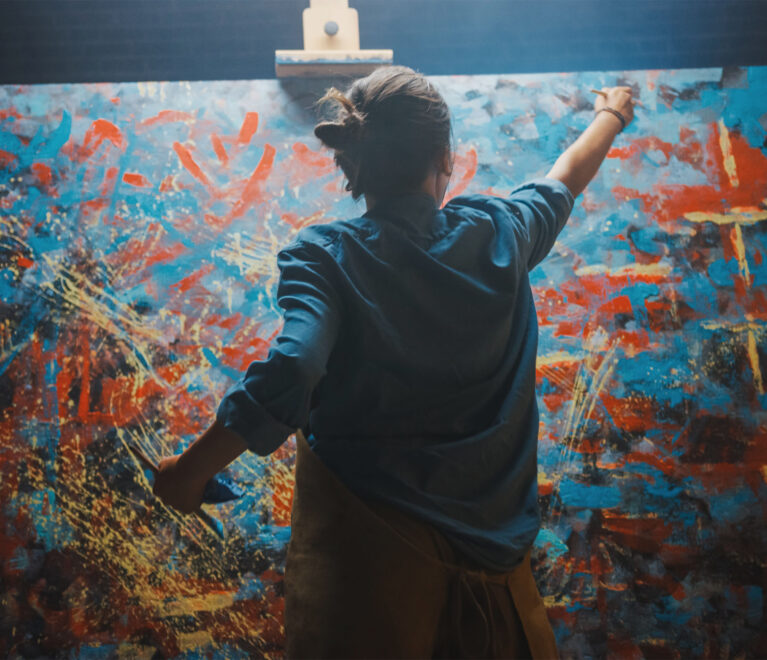 Talented Female Artist Works on Abstract Oil Painting, Using Paint Brush She Creates Modern Masterpiece. Dark and Messy Creative Studio where Large Canvas Stands on Easel Illuminated.