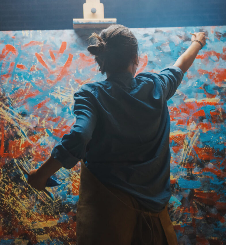 Talented Female Artist Works on Abstract Oil Painting, Using Paint Brush She Creates Modern Masterpiece. Dark and Messy Creative Studio where Large Canvas Stands on Easel Illuminated.