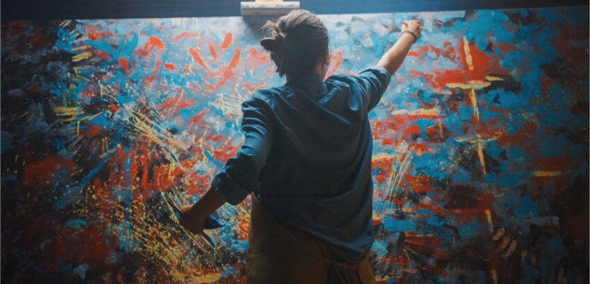 Talented Female Artist Works on Abstract Oil Painting, Using Paint Brush She Creates Modern Masterpiece. Dark and Messy Creative Studio where Large Canvas Stands on Easel Illuminated.