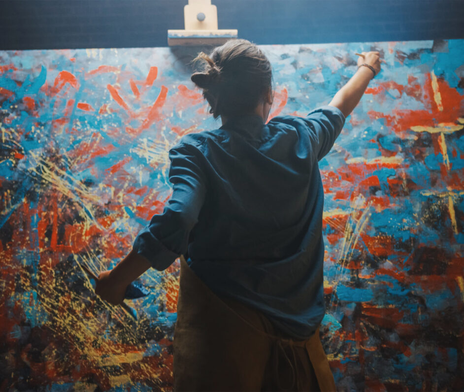 Talented Female Artist Works on Abstract Oil Painting, Using Paint Brush She Creates Modern Masterpiece. Dark and Messy Creative Studio where Large Canvas Stands on Easel Illuminated.